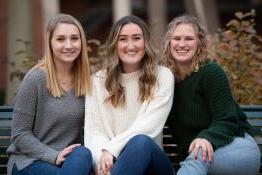 three students sitting and smiling